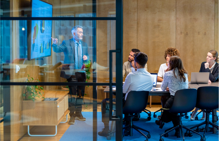 Multiple people in a conference room and one man is presenting a presentation